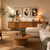 A beautifully styled modern living room featuring a cream sectional sofa, a round wooden coffee table, a mid-century modern wooden credenza, and three framed abstract art prints on the wall.
